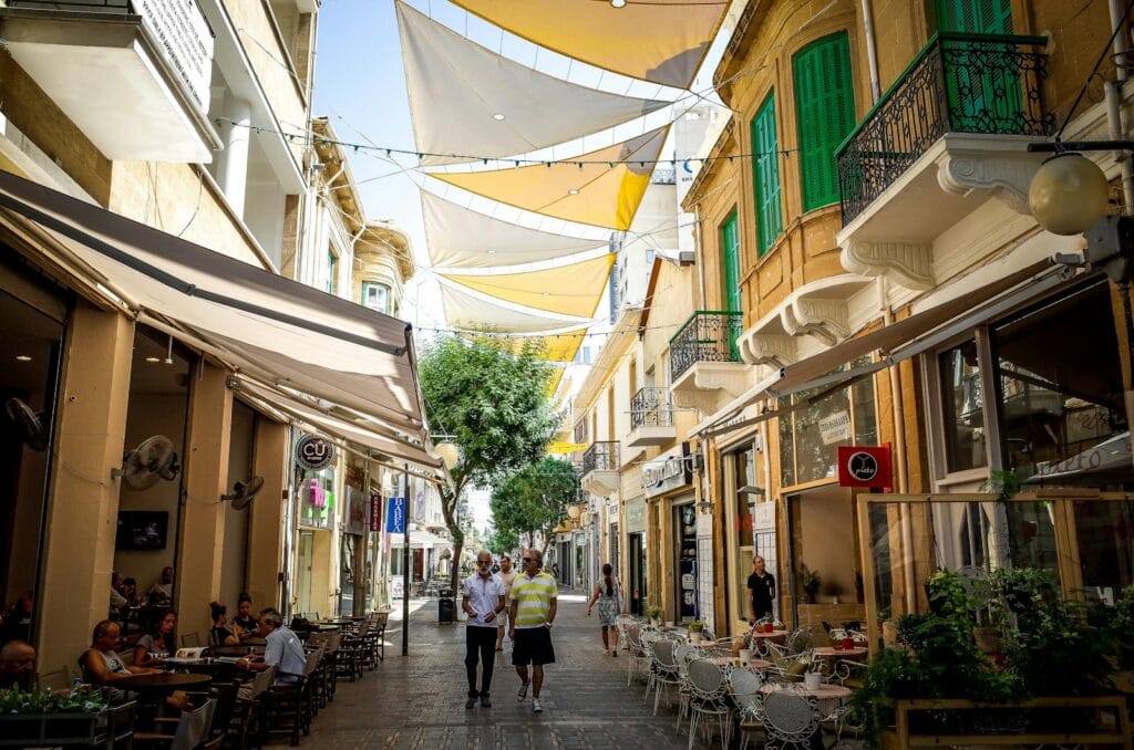 Bustling street in Nicosia, Cyprus with cafes, shops, and people under colorful shades.